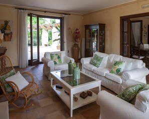 Ein geräumiges Wohnzimmer mit weißen Sofas, einem Glastisch und einem Korbstuhl.