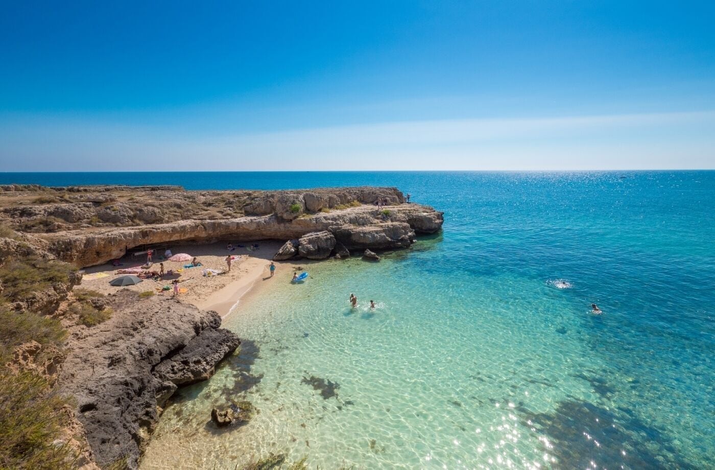 A coastal beach with clear water, rocky formations, and people enjoying the beach.