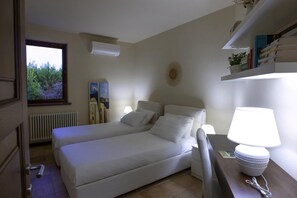 A hotel room with a bed, bedside table, lamp, radiator, and a window with a view of trees. - Villa Monica - Private Spacious Villa with 15m Pool near Polignano a Mare (Bari)