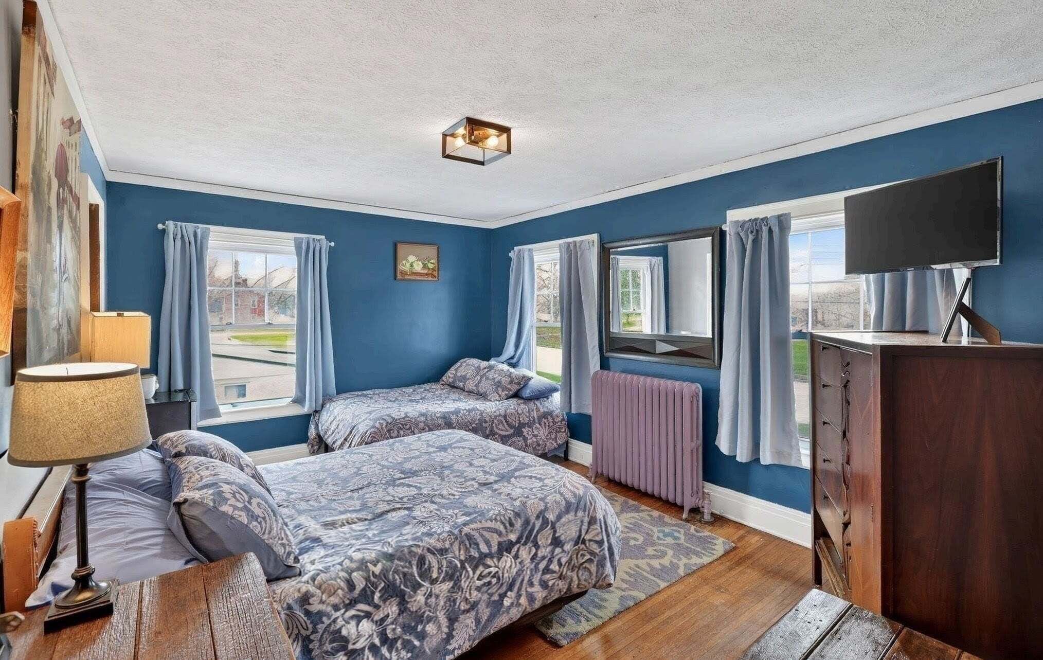 Une chambre avec deux lits, une commode, une télévision et une fenêtre avec des rideaux.