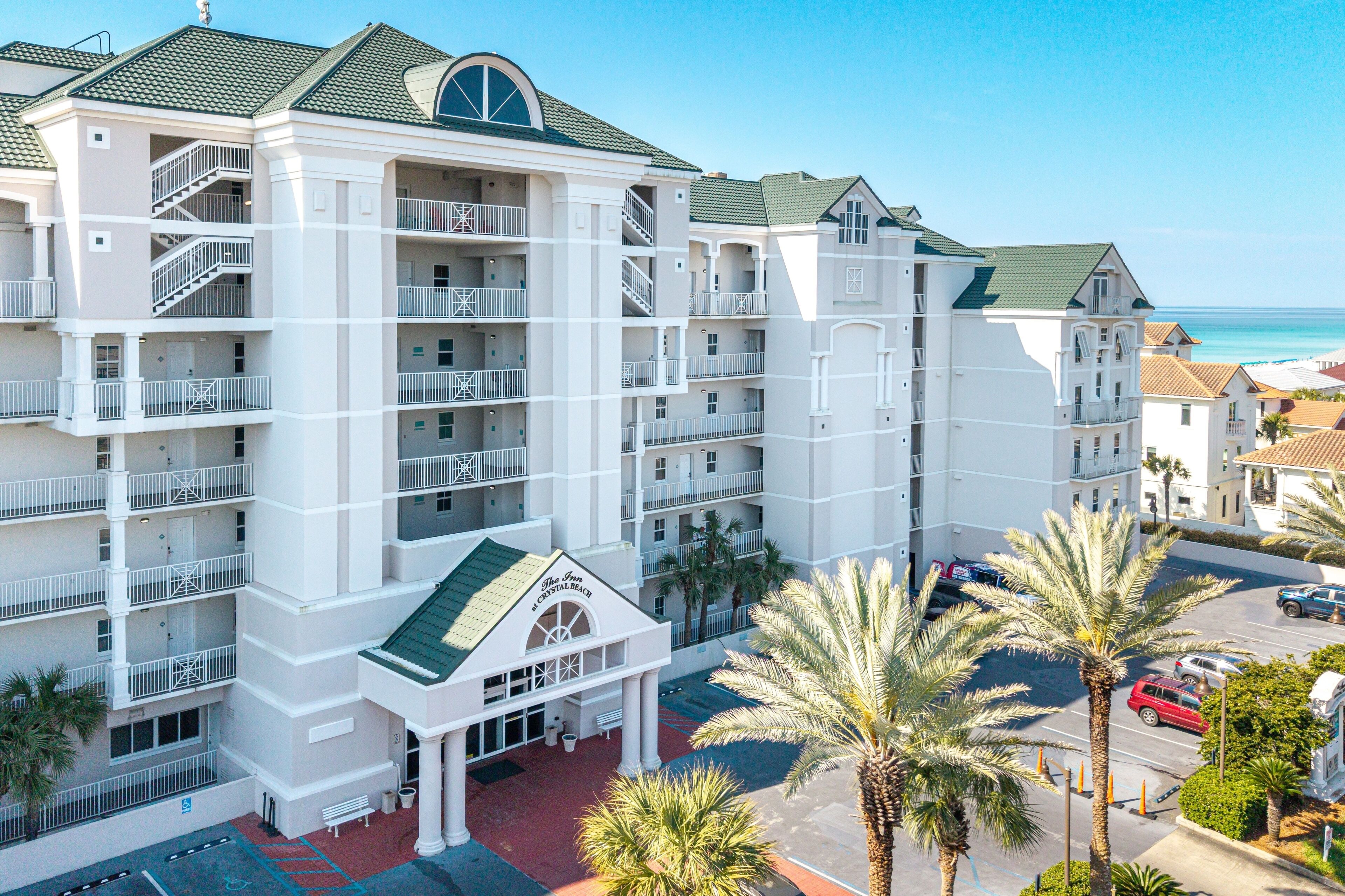 A multi-story hotel with balconies, a central entrance, and a parking area.