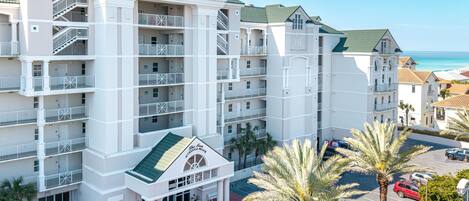 A multi-story hotel with balconies, a central entrance, and a parking area.
