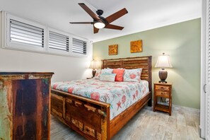 A bedroom with a wooden bed, two bedside tables with lamps, a ceiling fan, and a window with blinds. - Kihei Surfside, #512 1 Bedroom Condo (Kihei)