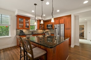 A modern kitchen with wooden cabinets, granite countertops, stainless steel appliances, and pendant lighting. - Kauai Pili Mai 4k 3 Bedroom Condo (Koloa)