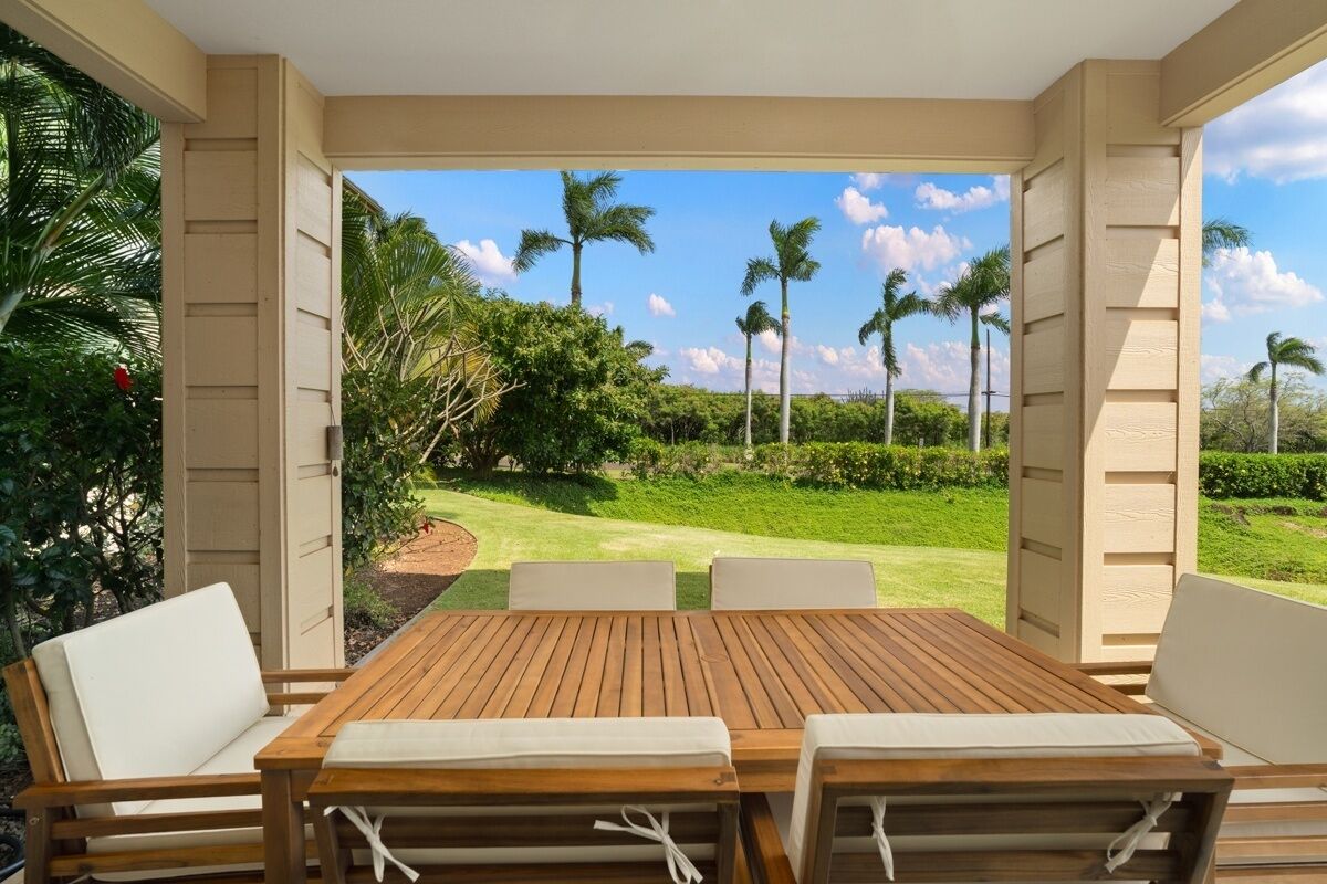 Una mesa de madera con cojines blancos, vista a un campo de golf y palmeras.