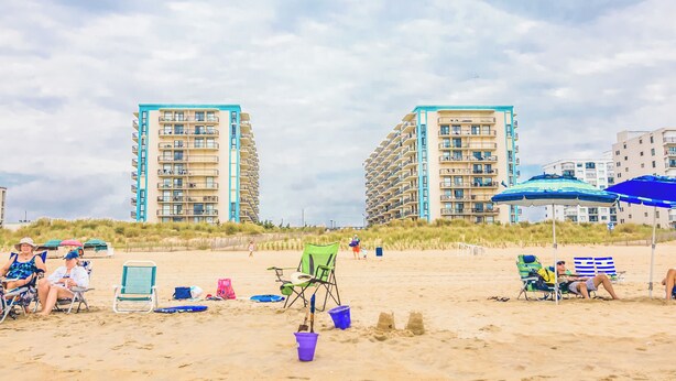 Ein Strand mit Liegestühlen, Sonnenschirmen und Sandburgen.