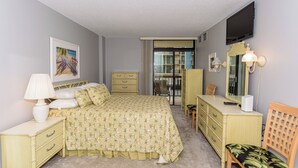 Ein Schlafzimmer mit einem Bett, einem Schminktisch, einem Sessel und einem an der Wand befestigten Fernseher.
