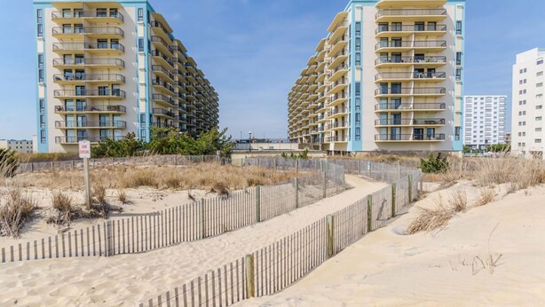 Un hôtel en bord de mer doté de nombreux balcons, une plage de sable en premier plan et un ciel dégagé.