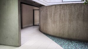 Um corredor com parede de concreto, chão ladrilhado e pequena área revestida com azulejos.