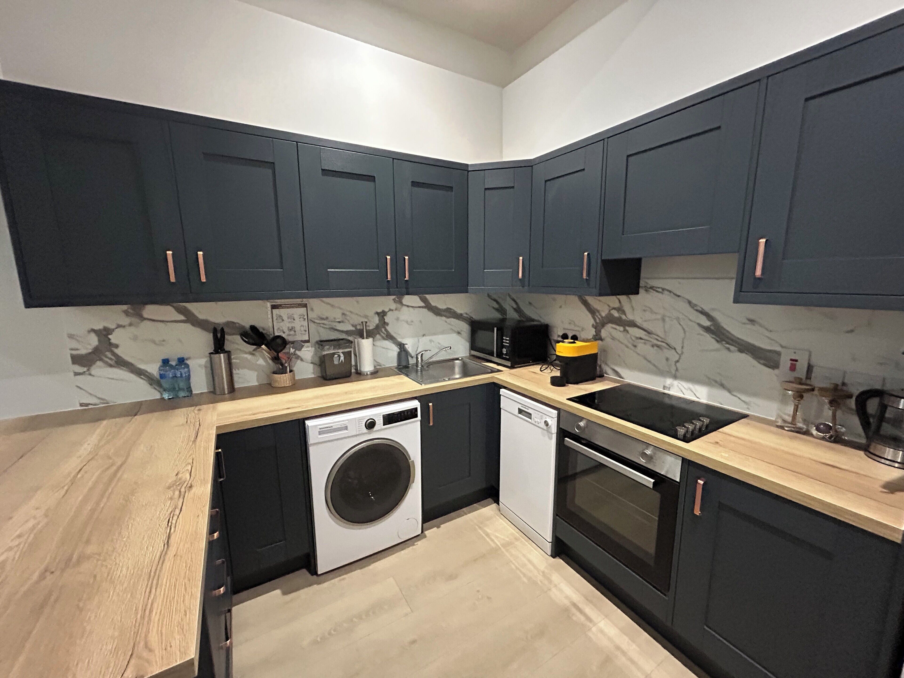 A modern kitchen with dark cabinets, a washing machine, a dishwasher, and a stove.