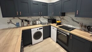 Une cuisine moderne avec des meubles de couleur sombre, un lave-linge, un lave-vaisselle et une cuisinière.