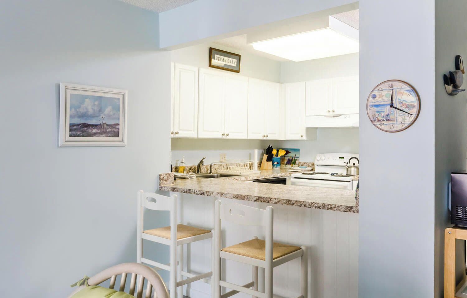 A kitchen with white cabinets, a marble countertop, a sink, a stove, and two bar stools.