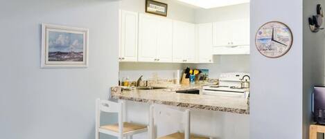 A kitchen with white cabinets, a marble countertop, a sink, a stove, and two bar stools.