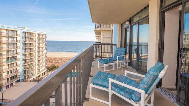 A balcony with a view of the beach, white chairs, and a glass door. - Oceanfront Building With Great Ocean and Bay Views (Ocean City)