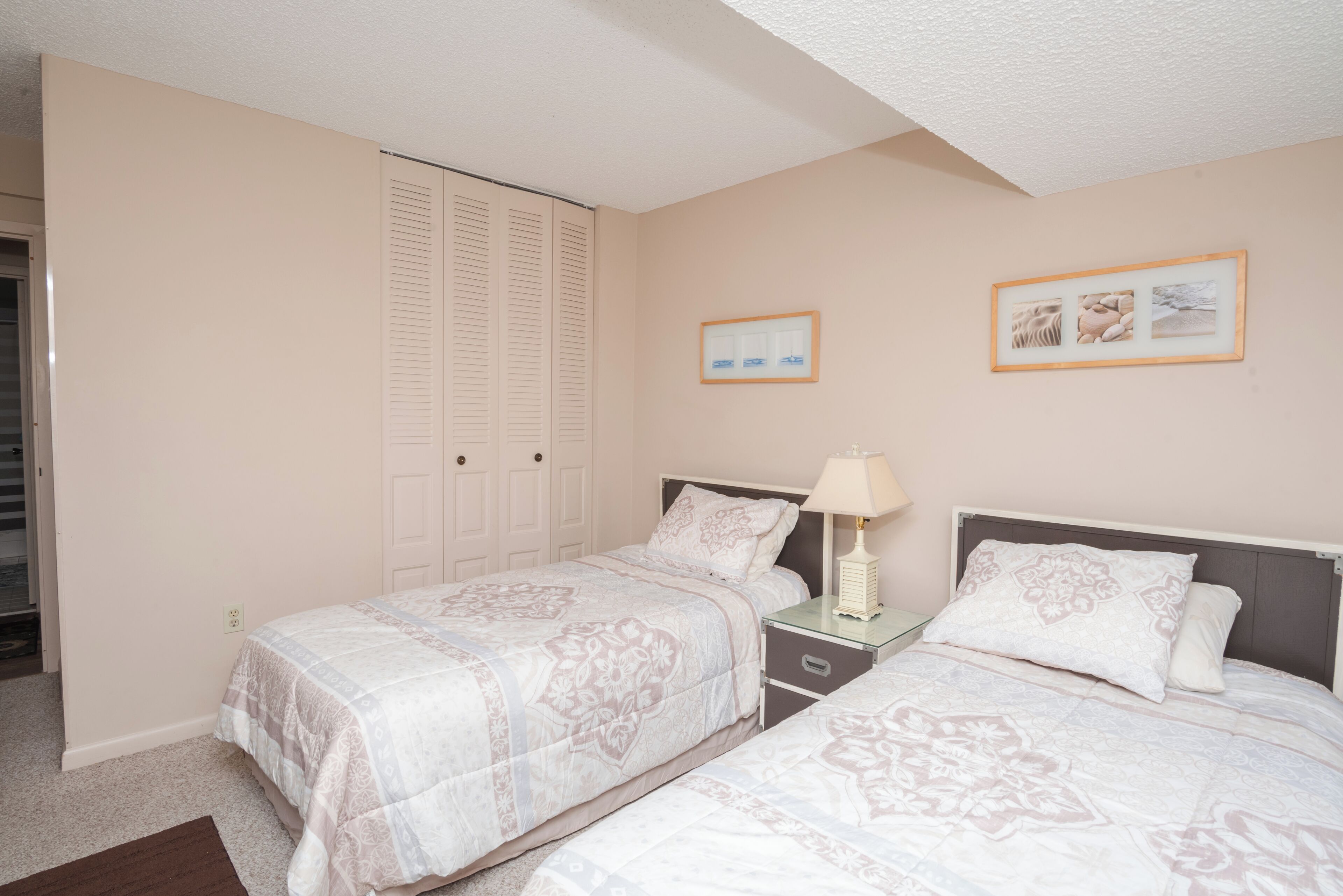 A bedroom with two beds, a nightstand, a lamp, and a closet.