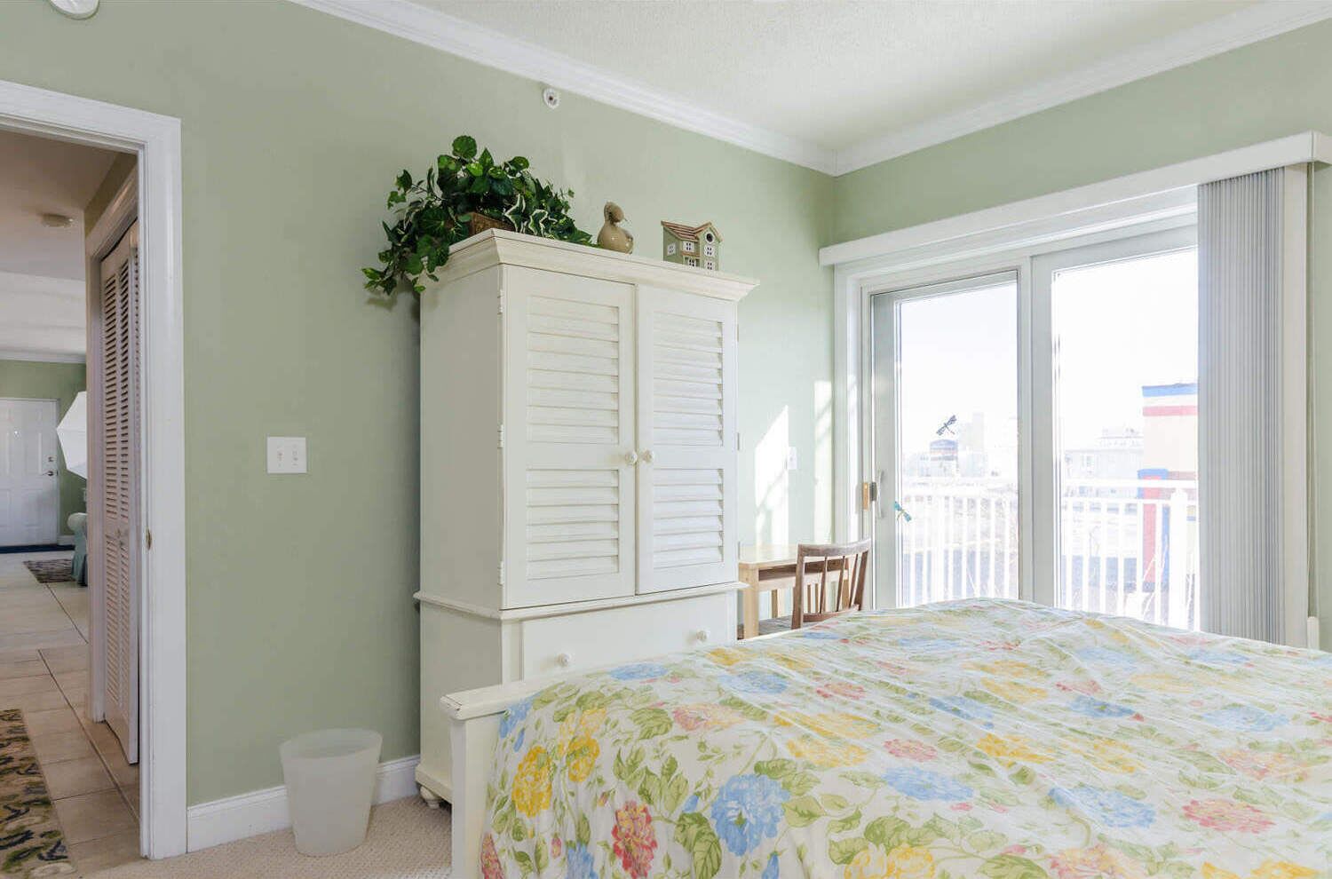 A bedroom with a bed, a white wardrobe, a window with a view, and a door leading to another room.