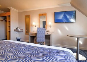 Hotellihuone, jossa on sänky, työpöytä, tuoli, televisio ja pieni pöytä.