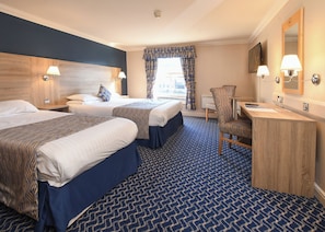 A hotel room with two beds, a desk with a chair, a mirror, and a window with curtains. - The Queens Hotel and Victoria Cloisters (York)