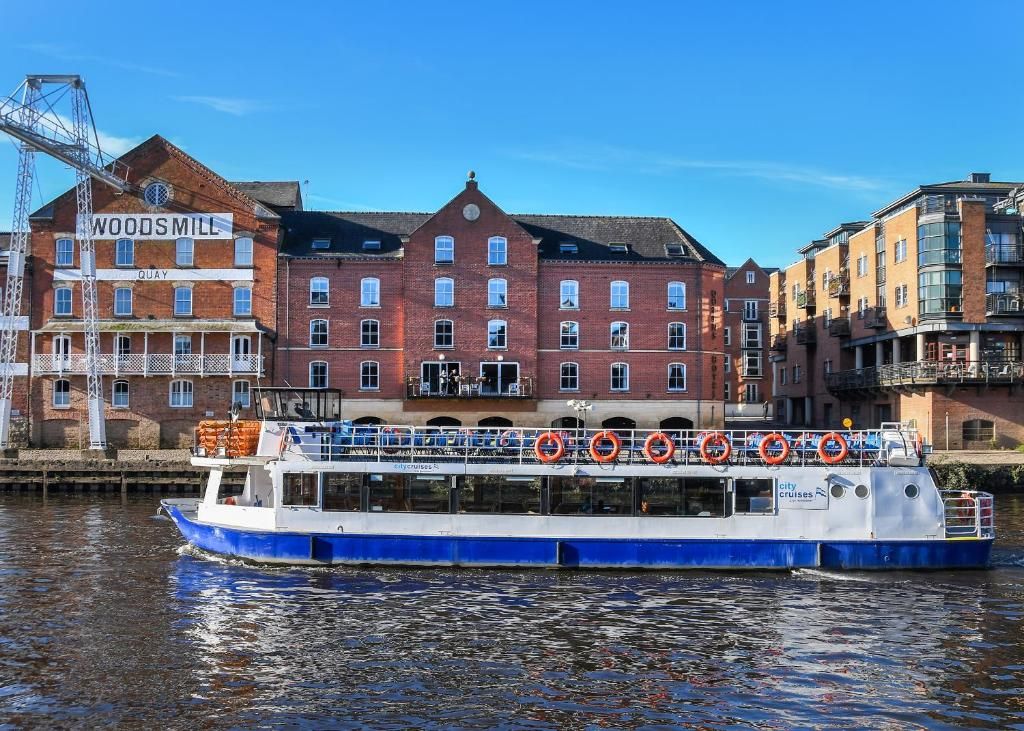 A blue and white boat with lifebuoys on the deck, docked near a red brick building labeled 'WOODSMILL QUAY'.