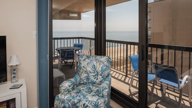 Un balcón con una silla, una mesa y vista al mar.