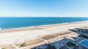 A beach view with a sandy shoreline, a clear sky, and a pool area with a fence. - Ocean City's Premiere Building (Ocean City)