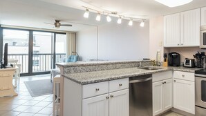 A modern kitchen with white cabinets, a granite countertop, a built-in dishwasher, and a coffee maker. - Ocean City's Premiere Building (Ocean City)