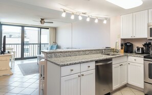 A modern kitchen with white cabinets, a granite countertop, a built-in dishwasher, and a coffee maker. - Ocean City's Premiere Building (Ocean City)