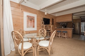 A wooden-paneled room with a glass-top dining table surrounded by wicker chairs, a kitchen area with stainless steel appliances, and a mounted flat-screen TV. - Large Oceanside Townhouse (Ocean City)