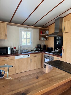 A compact kitchen with wooden cabinets, a microwave, a dishwasher, a sink, and a stove. - La Parenthèse enchantée (Le Vast)
