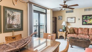 A dining area with a glass table, wicker chairs, a ceiling fan, and a sofa with floral upholstery. - Oceanfront Building With Great Ocean and Bay Views (Ocean City)