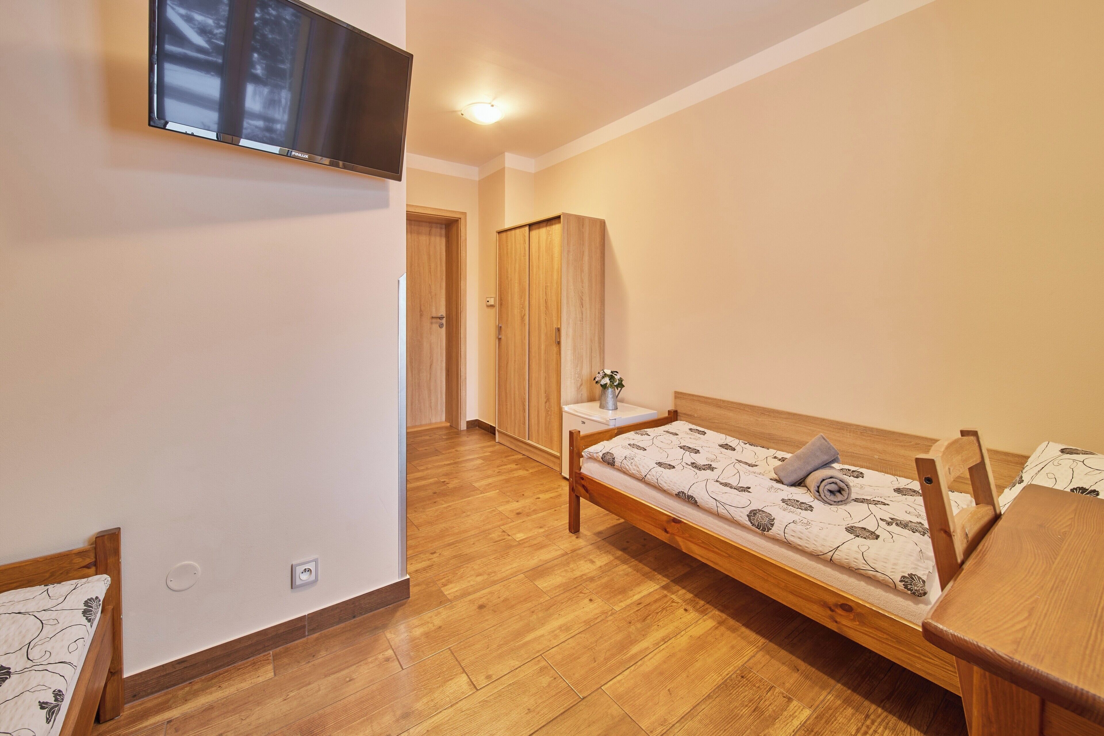 A bedroom with a wooden bed, a bedside table, a TV mounted on the wall, and a wardrobe.