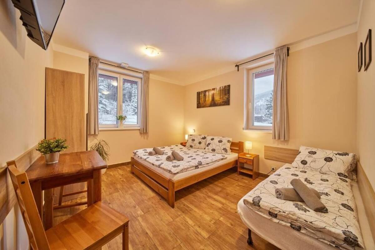 A cozy bedroom with a wooden bed, a small desk, and a window with a view of trees.