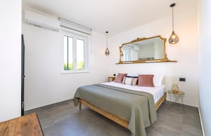 Um quarto com uma cama, um espelho grande, uma janela e uma mesa de cabeceira.