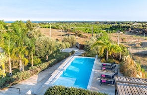 Ein rechteckiger Swimmingpool mit glasklar blauem Wasser, umgeben von einer Betonplattform. Entlang des Poolrandes sind Liegestühle mit rosafarbenen Kissen aufgereiht.