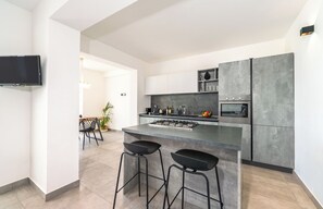 Eine moderne Küche mit Kochinsel, Barhocker, Edelstahlgeräten und einem flachbildfernseher an der Wand.