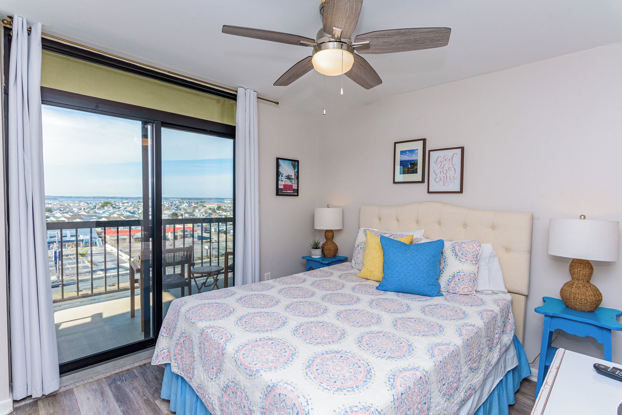 A hotel room with a large bed, a ceiling fan, a balcony with a view, and a cityscape.