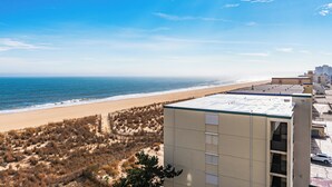 Een gebouw aan de kust met een plat dak, naast een strand met schaarse begroeiing en een heldere lucht.
