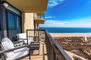 Un balcón con vista a la playa, una silla y una mesa.