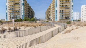 Een strandhotel met meerdere balkons, een zandstrand en een omheind pad.
