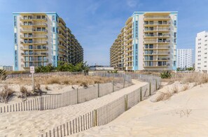 A beachfront hotel with multiple balconies, a sandy beach area, and a fenced walkway. - Oceanfront Building With Great Ocean and Bay Views (Ocean City)