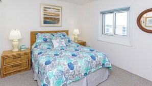 A bedroom with a bed, two bedside tables, a window, and a wall-mounted picture.