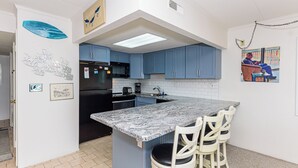 A kitchen with blue cabinets, a black refrigerator, a marble countertop, and a small island with chairs.