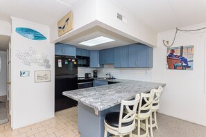A kitchen with blue cabinets, a black refrigerator, a marble countertop, and a small island with chairs. - Great views from this oceanfront side view unit (Ocean City)