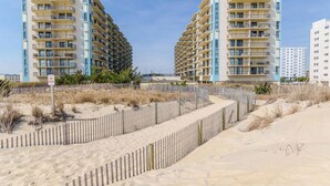 Un hotel frente a la playa con varios balcones, una playa arenosa en primer plano y un cielo despejado.