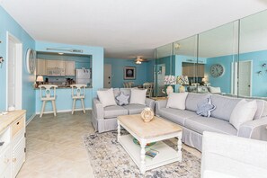 Ein Wohnzimmer mit grauem Sofa, einem Holztisch und einer Küche im Hintergrund.