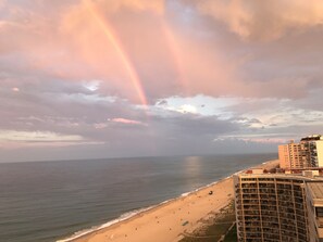 Una spiaggia con un arcobaleno, il mare e un edificio con balconi.