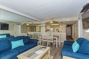 A living room with blue sofas, a wooden coffee table, and a kitchen in the background. - Ocean City's Premiere Building (Ocean City)