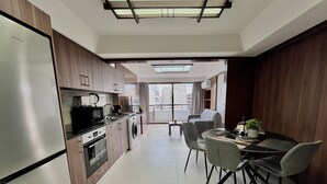 Una cocina moderna con electrodomésticos integrados, un comedor con mesa y sillas, y vistas de la ciudad a través de amplios ventanales.