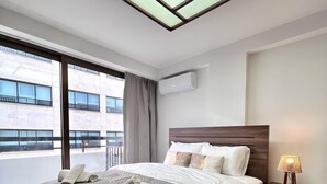 Habitación de hotel con una cama grande, una mesita de noche con lámpara, un equipo de aire acondicionado y vistas al exterior.