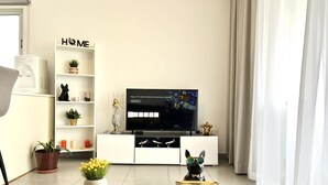A modern living room with a flat-screen TV, a glass coffee table, a decorative dog figurine, and a white shelving unit with plants and a 'HOME' sign. - 127 NIC - Stay Sun Line Apartment (Nicosia)